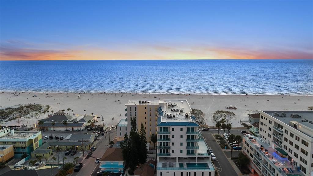 An aerial view shows a beach resort with a pool, nearby buildings, and the ocean — 15 AVALON STREET UNIT 502, CLEARWATER BEACH, FL