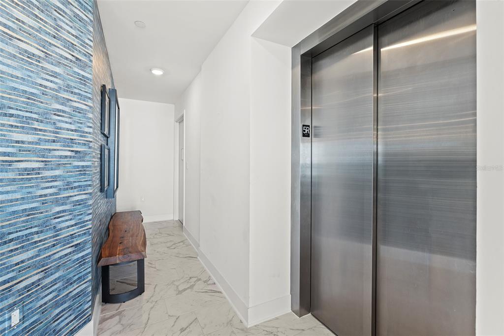 A hallway features a blue textured accent wall, a wooden bench, and stainless steel elevator doors — 15 AVALON STREET UNIT 502, CLEARWATER BEACH, FL
