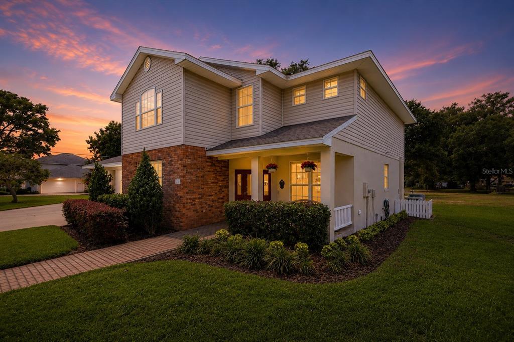 A two-story house with beige siding, a brick facade, and a covered front porch at sunset — 1503 AUBURN OAKS BOULEVARD, AUBURNDALE, FL