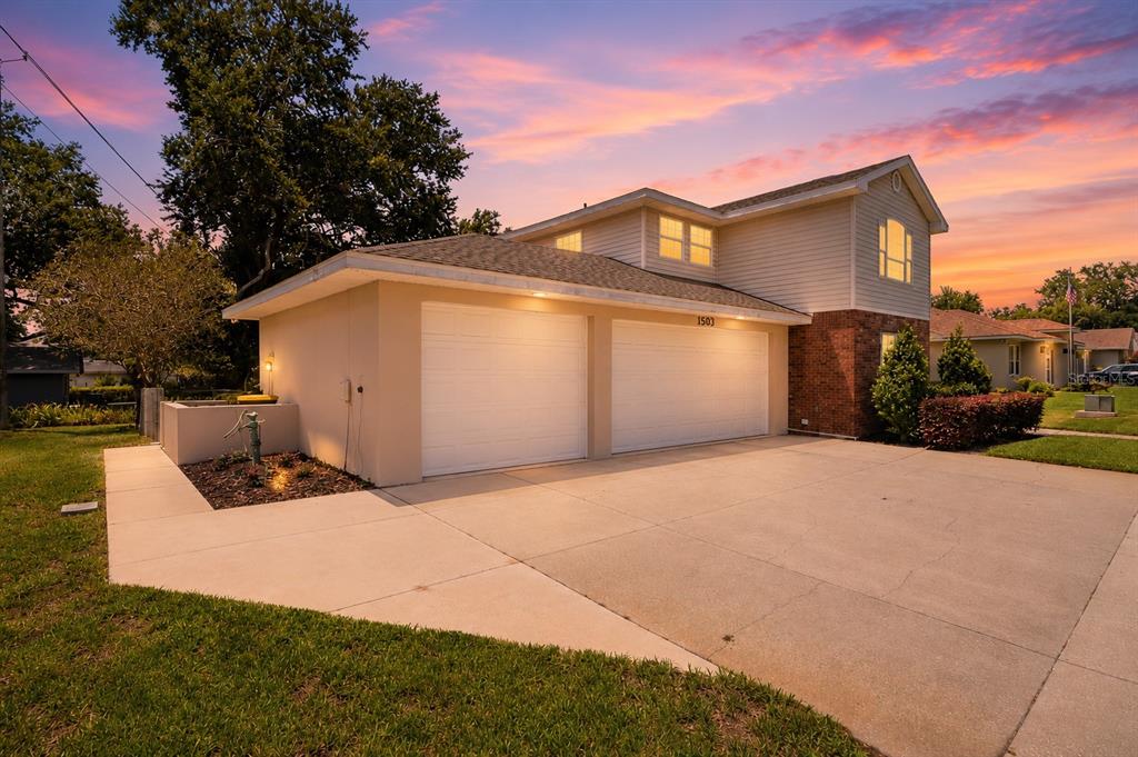 A two-story house features a two-car garage, light-colored siding, and a brick accent wall — 1503 AUBURN OAKS BOULEVARD, AUBURNDALE, FL