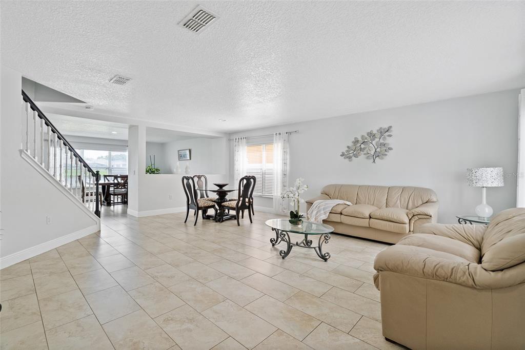 A living room with tile flooring, a beige sofa, and a dining area near stairs — 2730 AMANDA KAY WAY, KISSIMMEE, FL