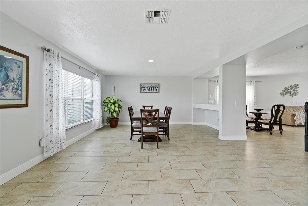 A dining room with tile flooring, a wooden table, and a large window with curtains — 2730 AMANDA KAY WAY, KISSIMMEE, FL
