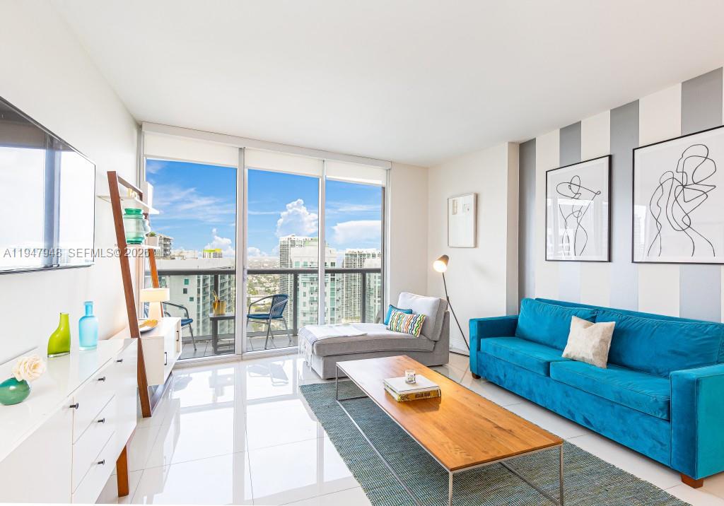 A modern living room features a blue sofa, a wooden coffee table, and floor-to-ceiling windows — 485 Brickell Ave # 4307, Miami FL 33131, MIAMI, FL