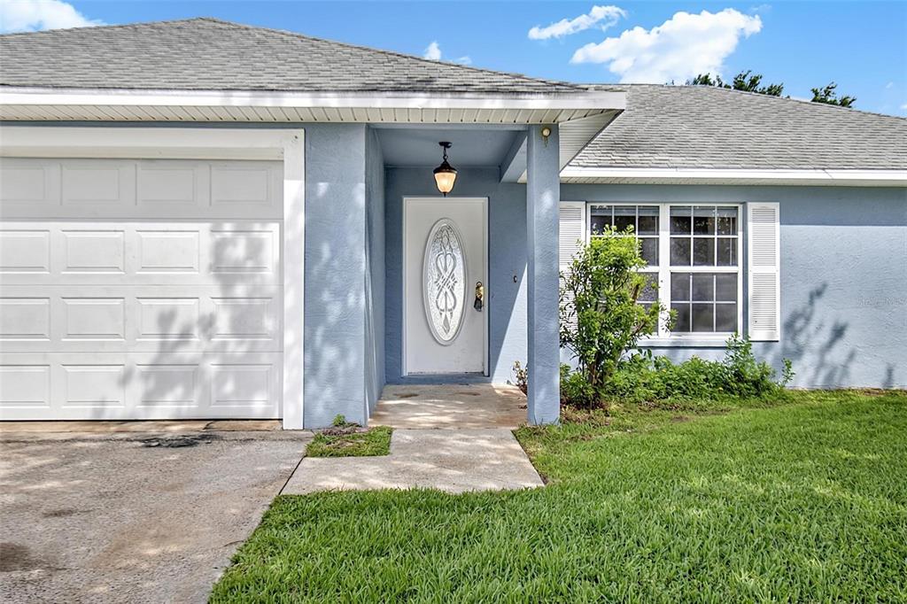 A light blue house exterior features a white garage door, front door, and shuttered window — 9 LYTTON LANE, PALM COAST, FL