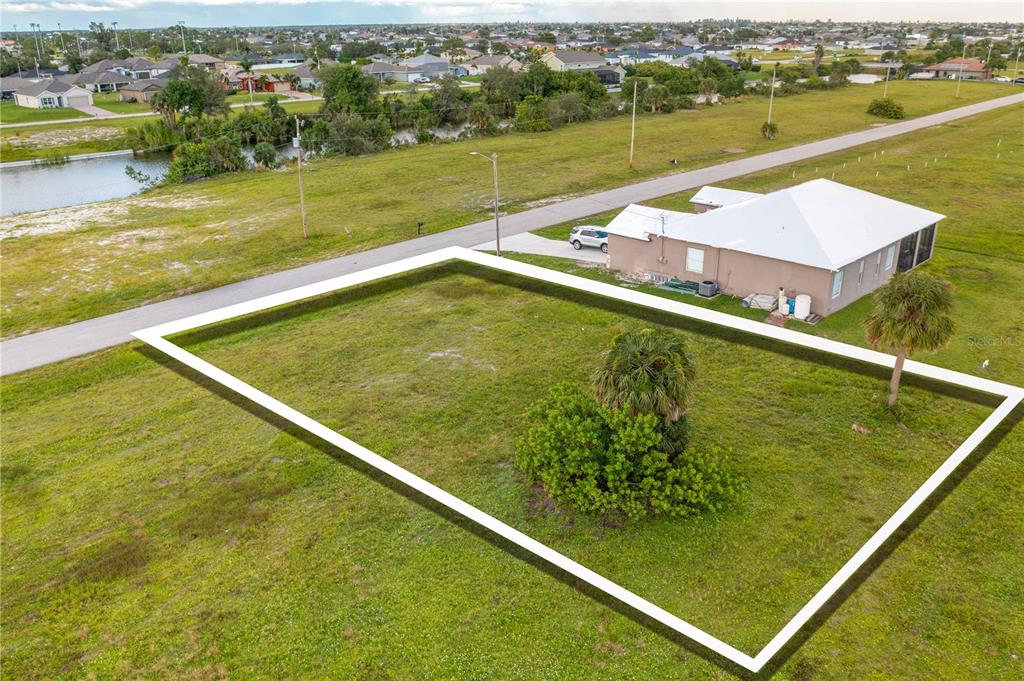 An aerial view shows a vacant, rectangular residential lot outlined in white next to a house — 1718 NW 8TH TERRACE, CAPE CORAL, FL