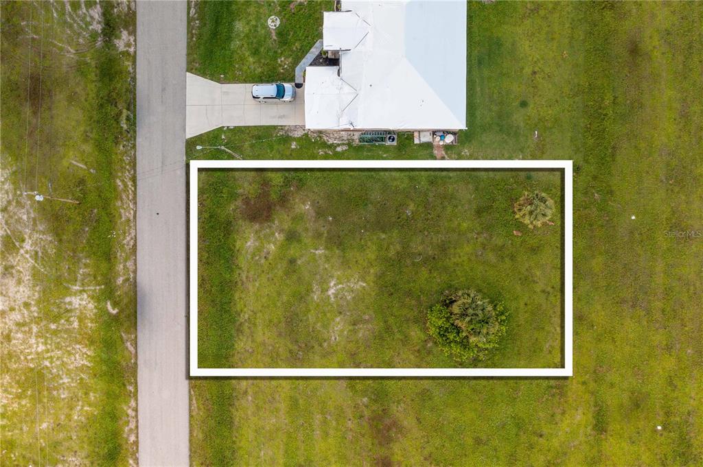 An aerial view shows a rectangular vacant lot outlined in white next to a house — 1718 NW 8TH TERRACE, CAPE CORAL, FL