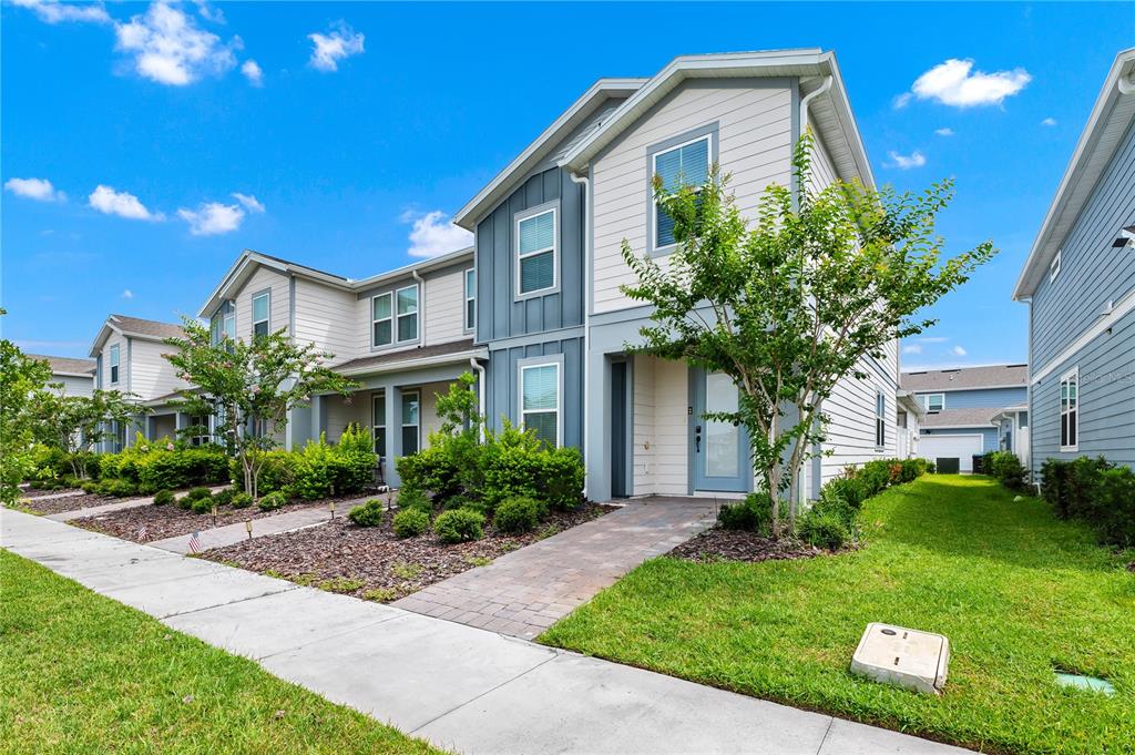 A two-story townhouse with light siding, blue accents, and a paved walkway leading to the entrance — 14253 LANIKAI BEACH DRIVE, ORLANDO, FL