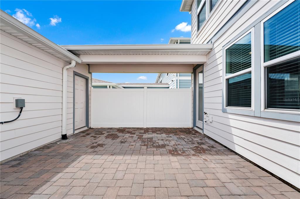 A paved patio area sits beneath a covered breezeway between two sections of a house — 14253 LANIKAI BEACH DRIVE, ORLANDO, FL