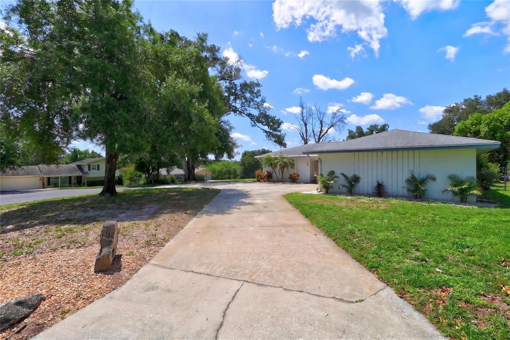 A concrete driveway leads to a single-story house with a light-colored exterior and landscaping — 54 LAKE LINK CIRCLE SE, WINTER HAVEN, FL