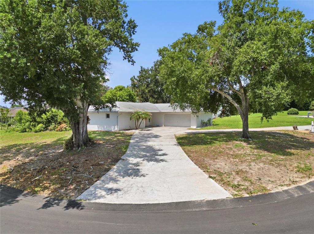 A single-story white house with a concrete driveway sits between two large oak trees — 54 LAKE LINK CIRCLE SE, WINTER HAVEN, FL