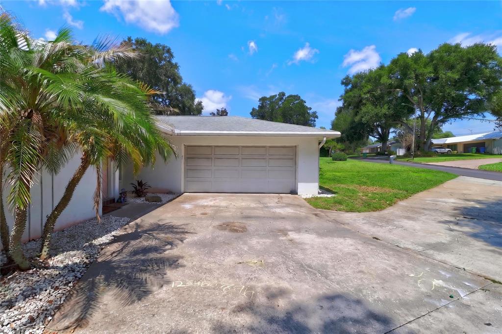 A white house exterior features a two-car garage, a concrete driveway, and a palm tree — 54 LAKE LINK CIRCLE SE, WINTER HAVEN, FL