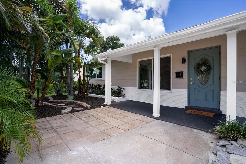 A front porch with a blue door, concrete patio, and landscaping under a cloudy sky — 6065 23RD AVENUE N, ST PETERSBURG, FL