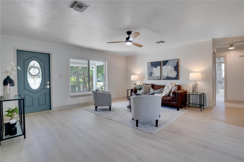 A living room features light wood flooring, a blue front door, and a brown leather sofa — 6065 23RD AVENUE N, ST PETERSBURG, FL