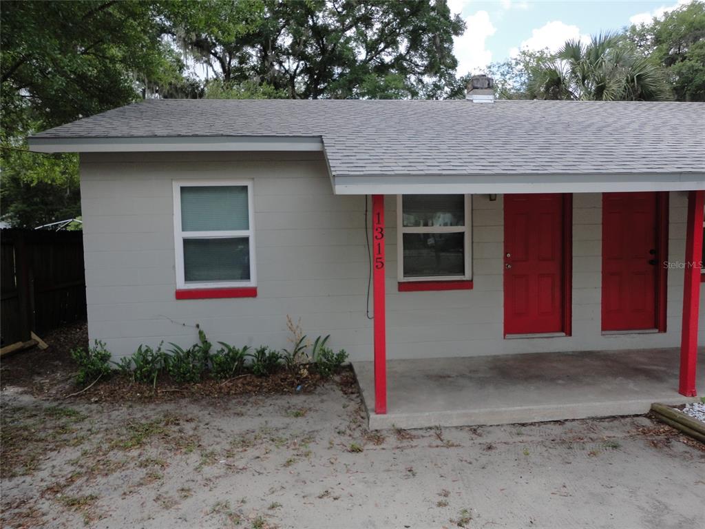 A single-story house exterior features gray siding, red doors, and a covered concrete porch — 1315 SE 3RD AVENUE, GAINESVILLE, FL