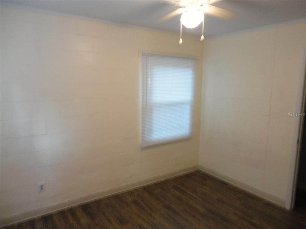 A small room features white block walls, wood-look flooring, a window with blinds, and a ceiling fan — 1315 SE 3RD AVENUE, GAINESVILLE, FL