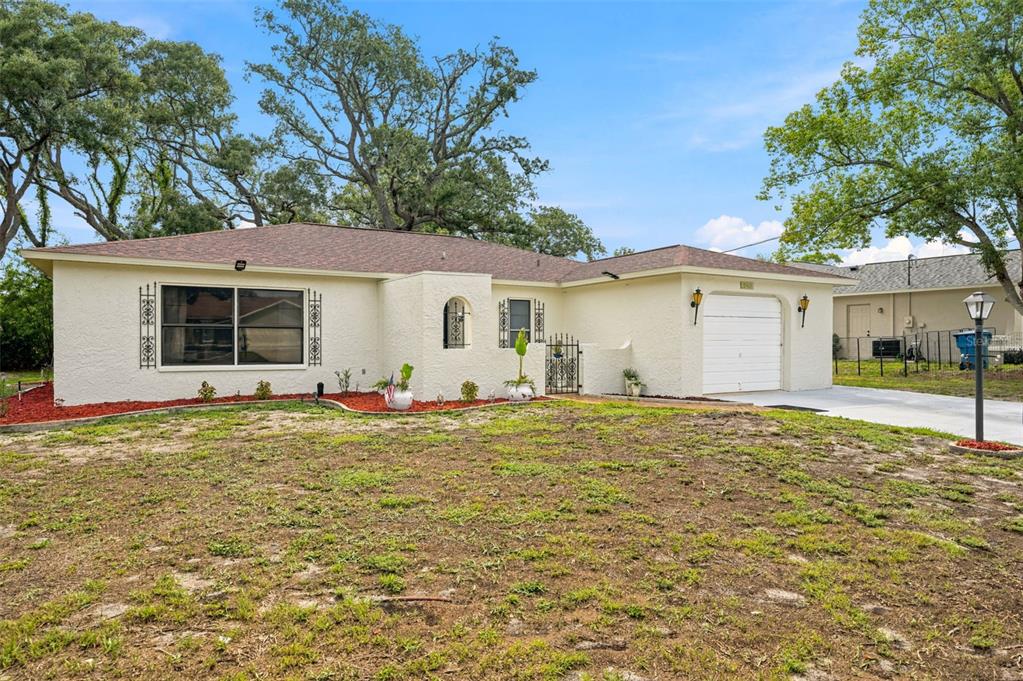 A single-story house with a white stucco exterior, a garage, and a large front yard — 5431 ALDERWOOD STREET, SPRING HILL, FL