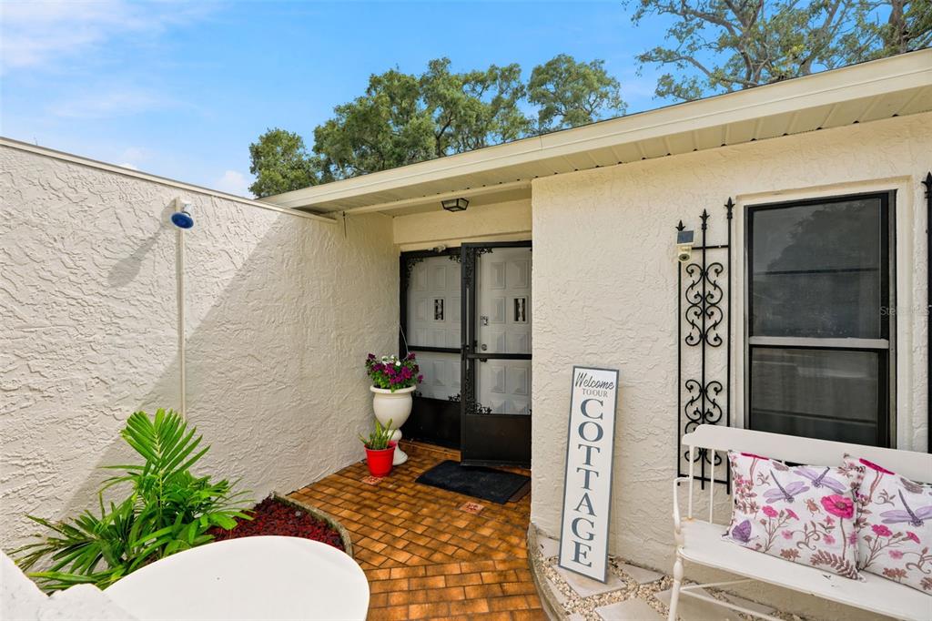 A brick-paved entryway features a white bench, a potted plant, and a cottage-themed sign — 5431 ALDERWOOD STREET, SPRING HILL, FL