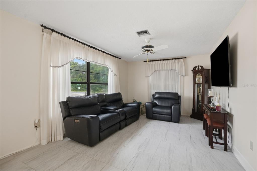 A living room features black leather seating, a grandfather clock, and light-colored tile flooring — 5431 ALDERWOOD STREET, SPRING HILL, FL