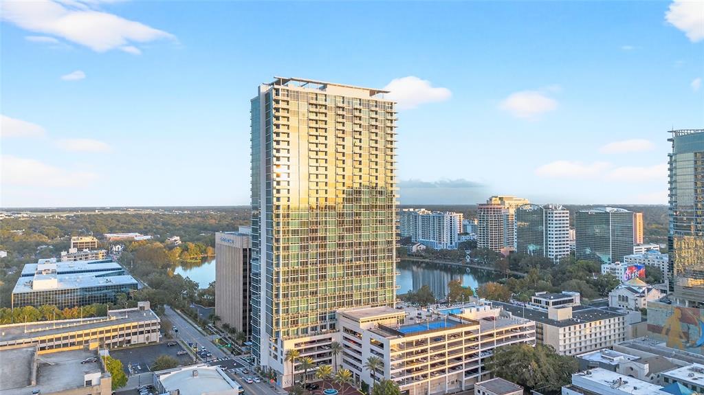 An aerial view shows a tall glass residential tower surrounded by city buildings and lakes — 150 E ROBINSON STREET UNIT 3106, ORLANDO, FL