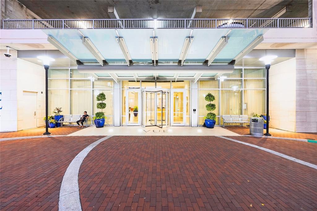 A brick driveway leads to the glass-enclosed entrance of a modern building with a canopy — 150 E ROBINSON STREET UNIT 3106, ORLANDO, FL