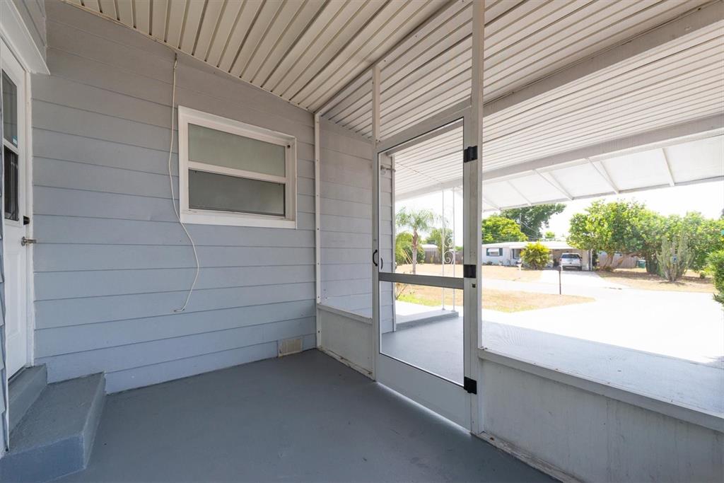 A gray-painted porch with a screen door and siding overlooks a driveway and yard — 11456 106TH STREET, LARGO, FL