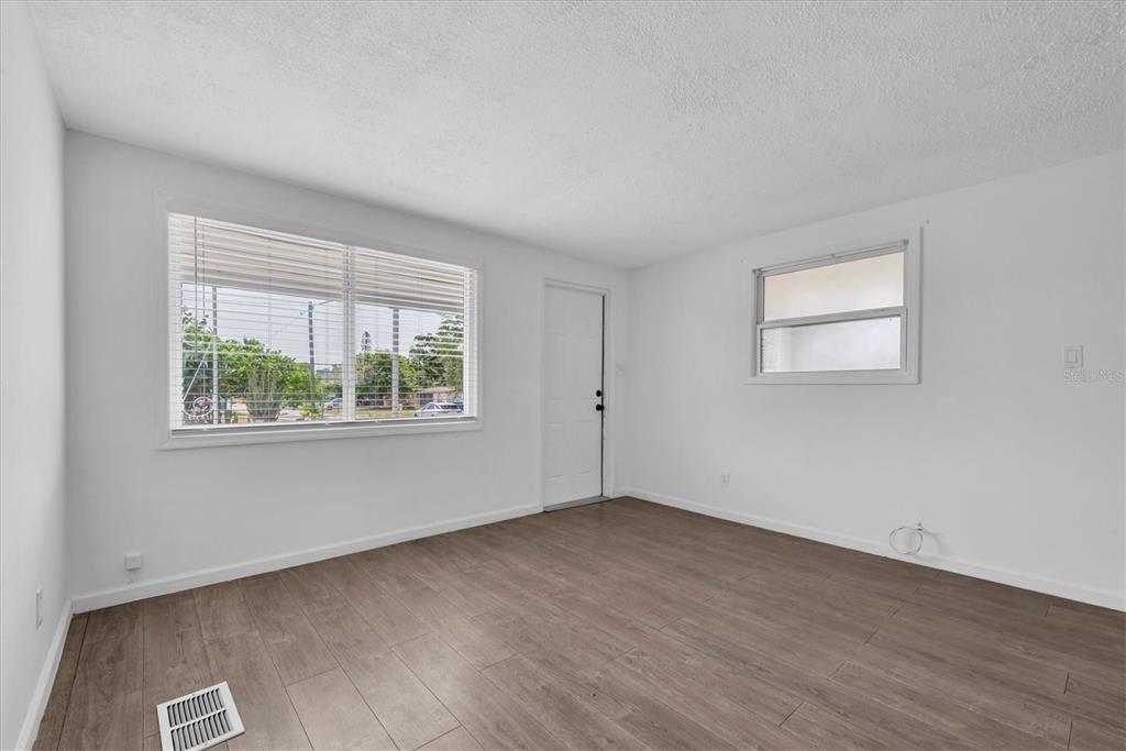 An empty room with white walls, wood-look flooring, a large window, and a white door — 11456 106TH STREET, LARGO, FL
