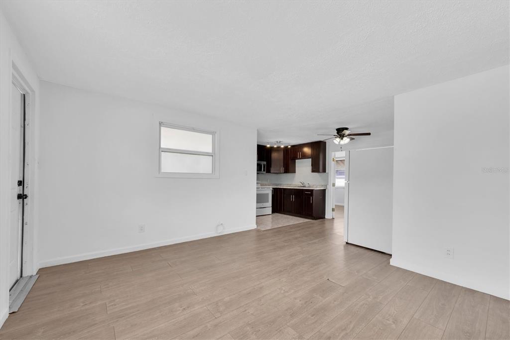 An open-concept living area features light wood-look flooring and a view into a dark-cabinet kitchen — 11456 106TH STREET, LARGO, FL