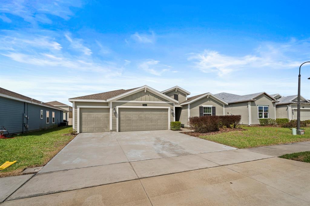 A single-story house with a tan exterior, a three-car garage, and a concrete driveway — 4327 LIGHTERKNOT TRACE, KISSIMMEE, FL