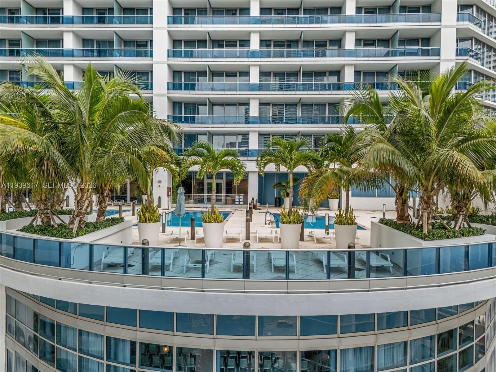 An outdoor pool deck with palm trees and lounge chairs overlooks a modern high-rise building — 200 Biscayne Boulevard Way # 4202, Miami FL 33131, MIAMI, FL