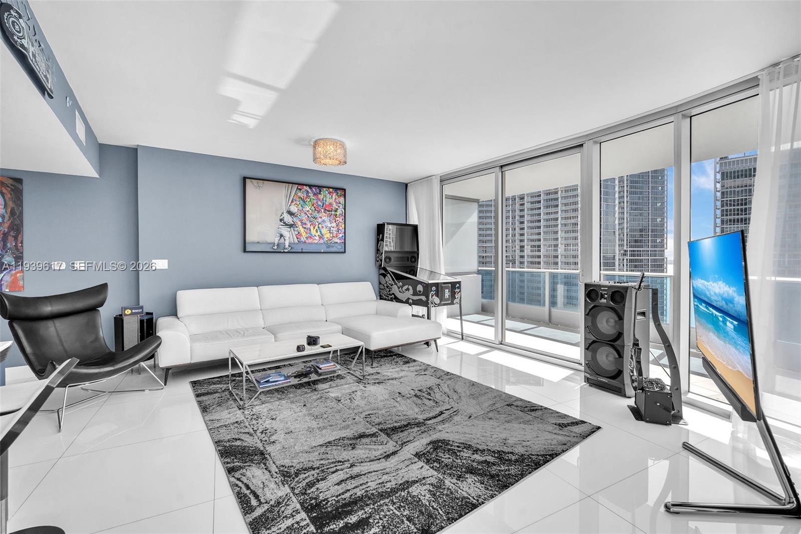 A modern living room features a white sectional sofa, a pinball machine, and floor-to-ceiling windows — 200 Biscayne Boulevard Way # 4202, Miami FL 33131, MIAMI, FL