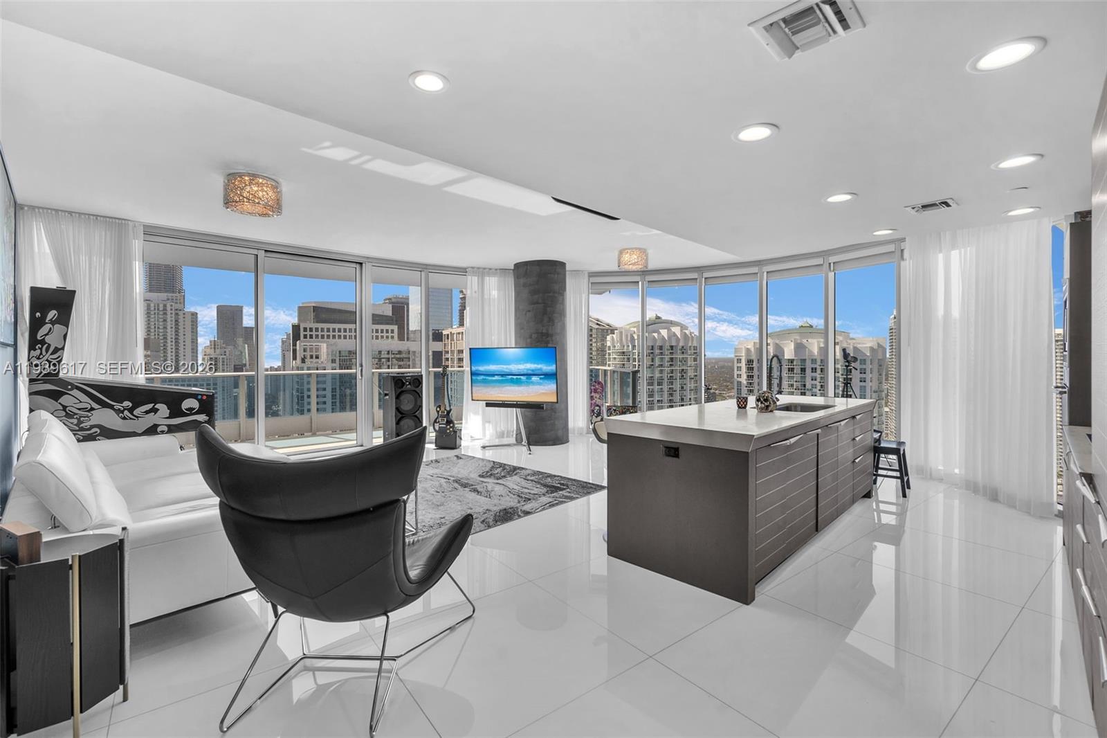 A modern open-concept living area features white tile floors, a kitchen island, and city views — 200 Biscayne Boulevard Way # 4202, Miami FL 33131, MIAMI, FL