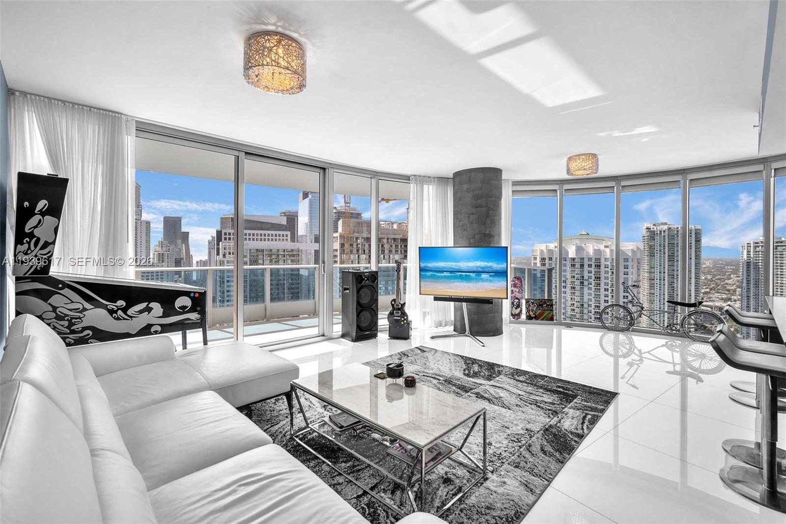 A modern living room features white tile floors, a sectional sofa, and floor-to-ceiling city views — 200 Biscayne Boulevard Way # 4202, Miami FL 33131, MIAMI, FL