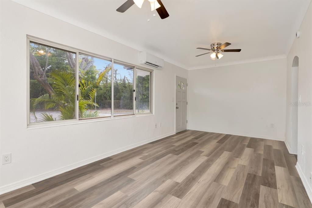 An empty room features light-colored walls, wood-look flooring, two ceiling fans, and large windows — 4939 HAINES ROAD N, ST PETERSBURG, FL