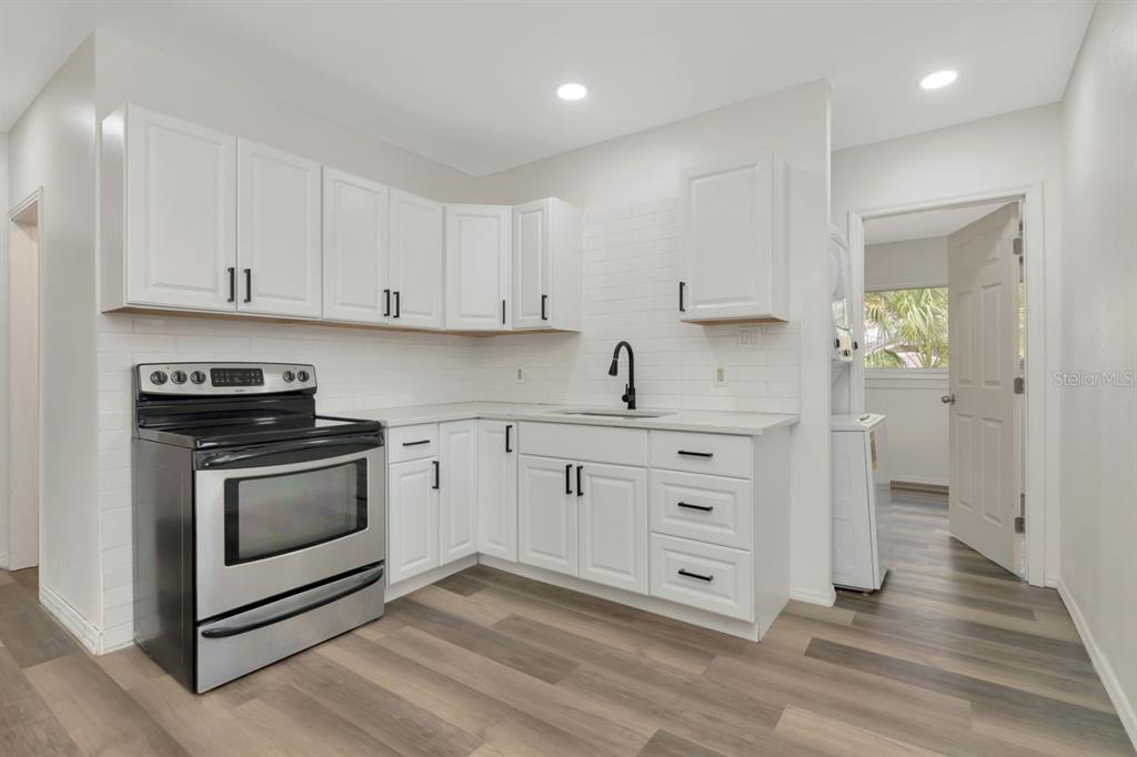 A kitchen with white cabinets, stainless steel appliances, white subway tile backsplash, and wood-look flooring — 4939 HAINES ROAD N, ST PETERSBURG, FL