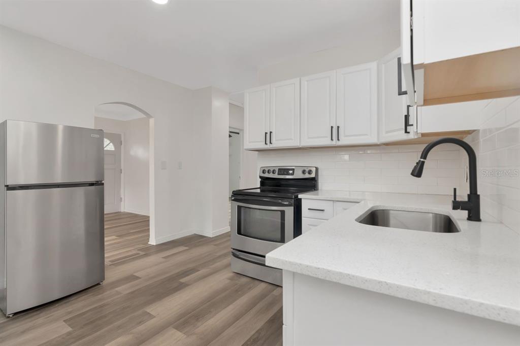 A kitchen features white cabinets, stainless steel appliances, a white countertop, and wood-look flooring — 4939 HAINES ROAD N, ST PETERSBURG, FL