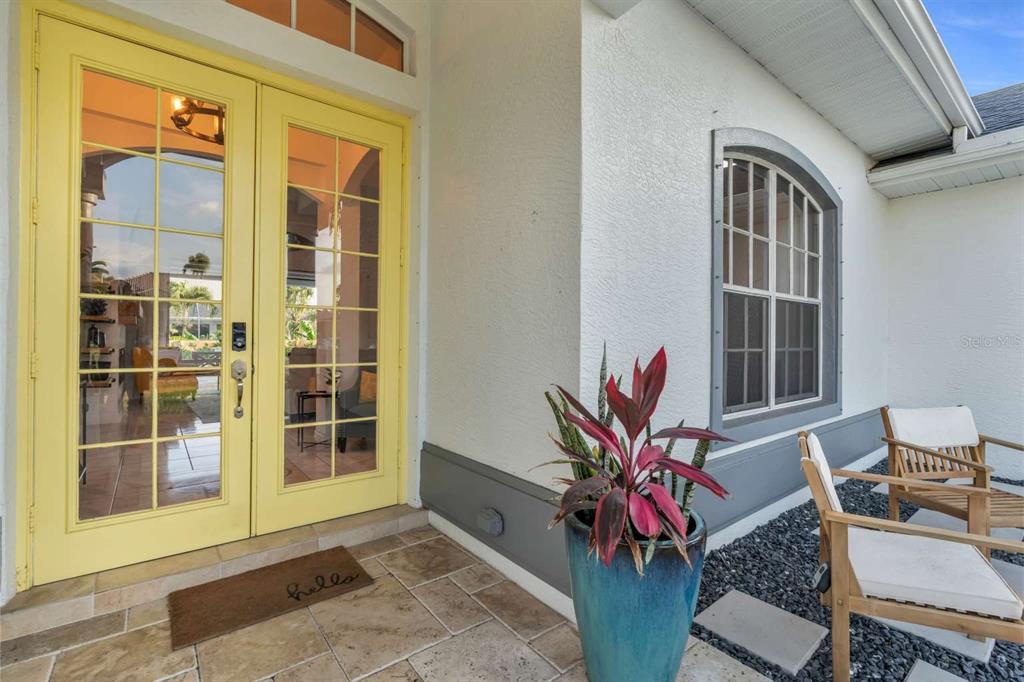 A yellow double door entrance features a tiled porch, a potted plant, and outdoor seating — 1720 SW 49TH LANE, CAPE CORAL, FL