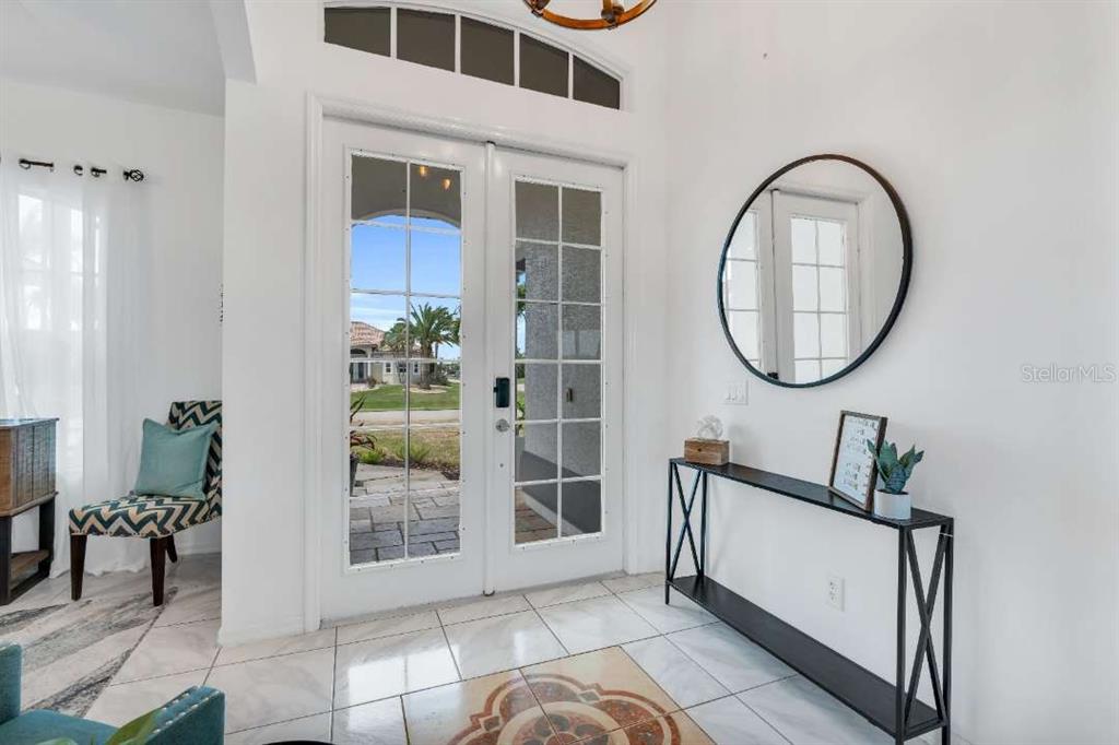 A bright entryway features white tile floors, a glass-paneled double door, and a console table — 1720 SW 49TH LANE, CAPE CORAL, FL
