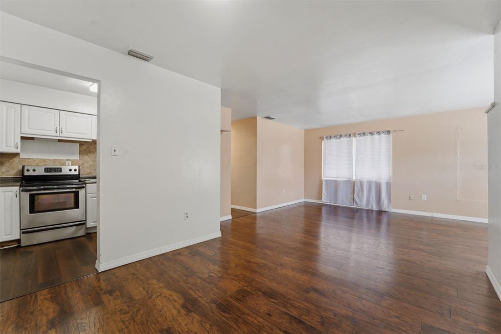 A view of a living room with wood-look flooring and an adjacent kitchen with white cabinets — 3235 EMERSON AVENUE S, ST PETERSBURG, FL