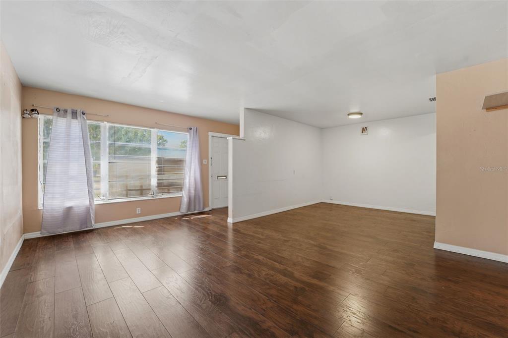 An empty living room features wood-look flooring, white walls, and a large window with curtains — 3235 EMERSON AVENUE S, ST PETERSBURG, FL