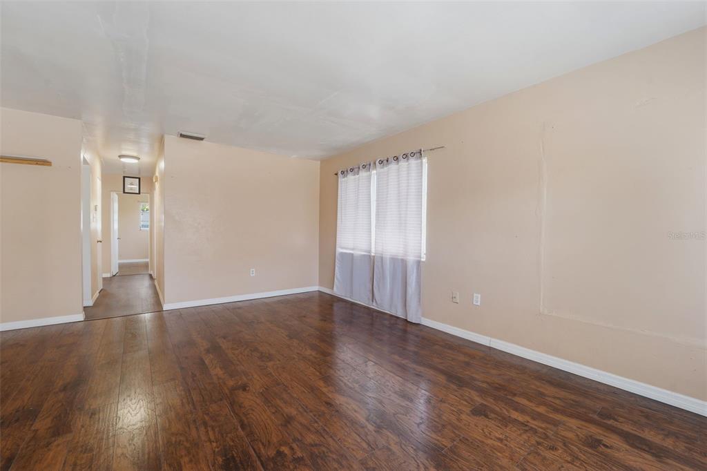 An empty room features dark wood-look flooring, light beige walls, and a window with curtains — 3235 EMERSON AVENUE S, ST PETERSBURG, FL