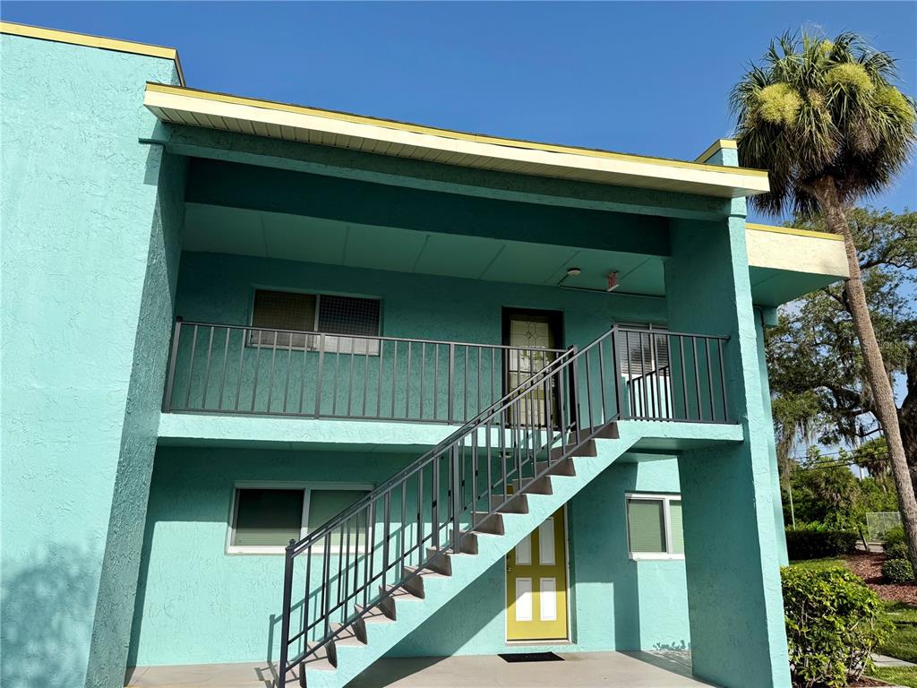 A two-story teal apartment building features an exterior staircase leading to an upper-level balcony — 1001 W EAU GALLIE BOULEVARD UNIT 217, MELBOURNE, FL