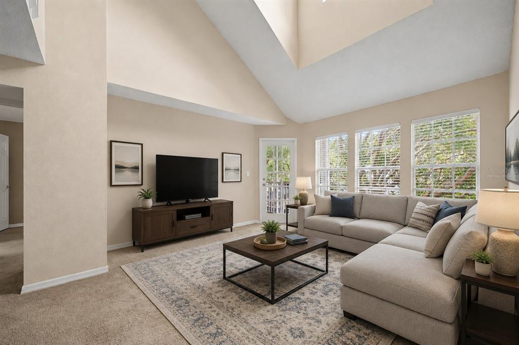 A living room with a vaulted ceiling, sectional sofa, television console, and large windows — 3270 HAVILAND COURT UNIT 301, PALM HARBOR, FL
