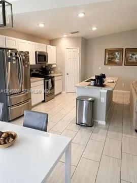 A kitchen with stainless steel appliances, white cabinetry, and a central island with a trash can — 2123 NE 6th Ave, Cape Coral FL 33909, CAPE CORAL, FL