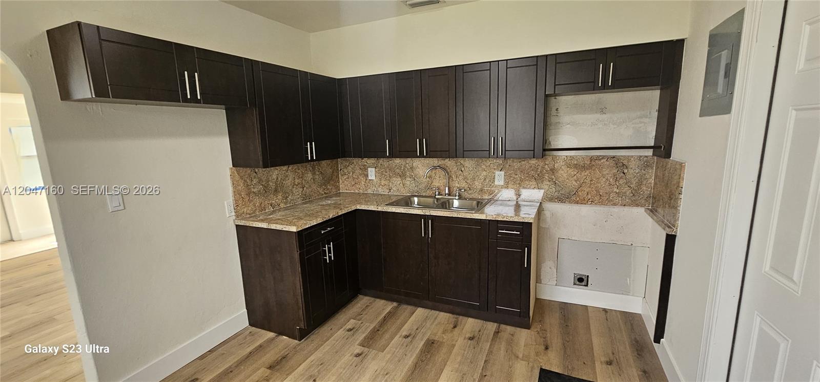 A kitchen features dark wood cabinets, a stone-patterned backsplash, and light wood-look flooring — 6010 SW 33rd St, Miramar FL 33023, MIRAMAR, FL