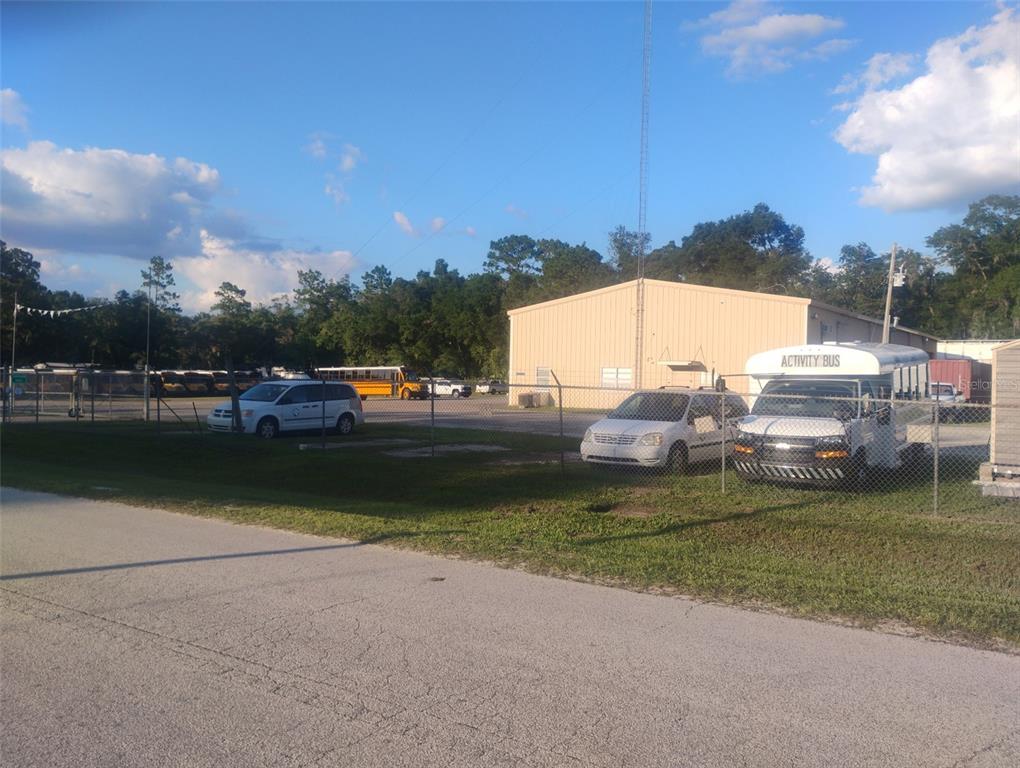 A grassy, undeveloped residential lot is framed by tall trees under a bright, sunny sky — 587 MARSHBURN DRIVE, BRONSON, FL