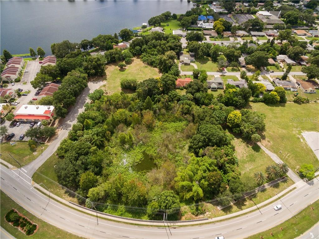 An aerial view shows a wooded lot with a pond situated between roads and houses — 1101 CYPRESS GARDENS BOULEVARD, WINTER HAVEN, FL