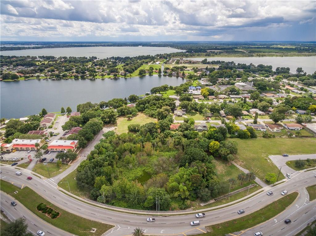 An aerial view shows a wooded vacant lot situated between a road and a lake — 1101 CYPRESS GARDENS BOULEVARD, WINTER HAVEN, FL