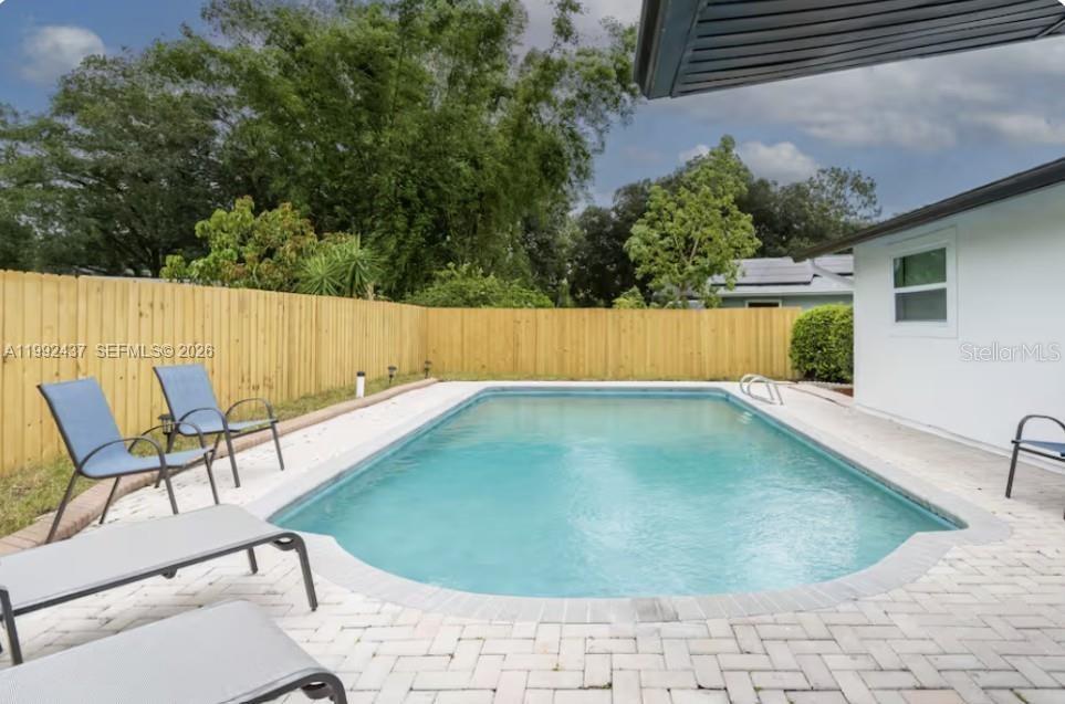 A rectangular swimming pool sits in a backyard patio area enclosed by a wooden fence — 8622 Baylor Cir, Orlando FL 32817, ORLANDO, FL