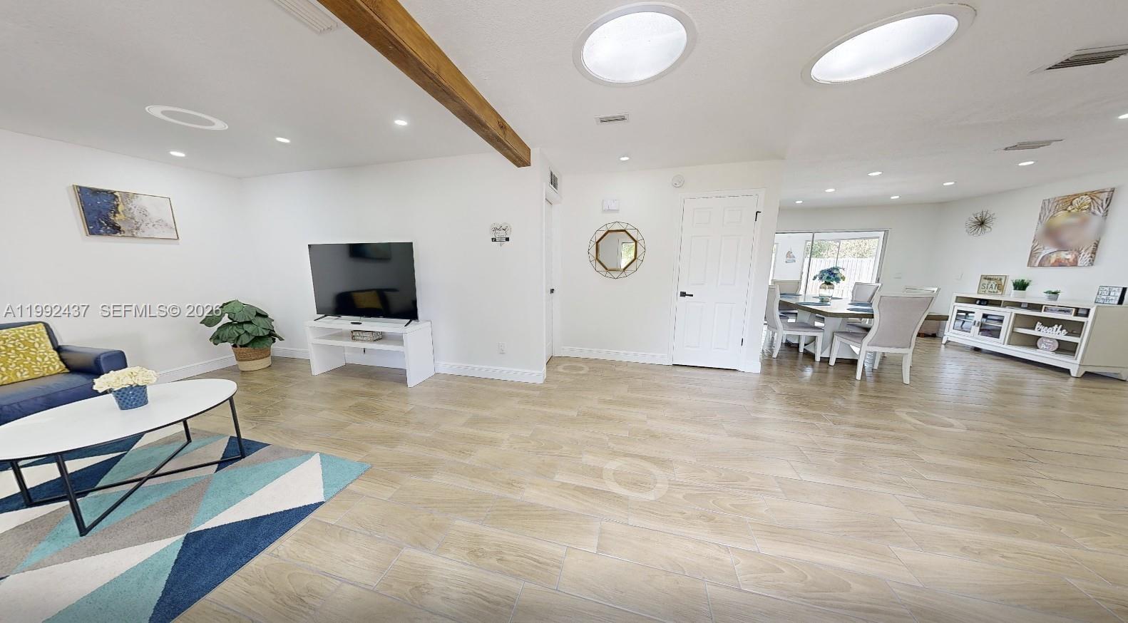 A living and dining area features light wood-look tile flooring and a wooden ceiling beam — 8622 Baylor Cir, Orlando FL 32817, ORLANDO, FL