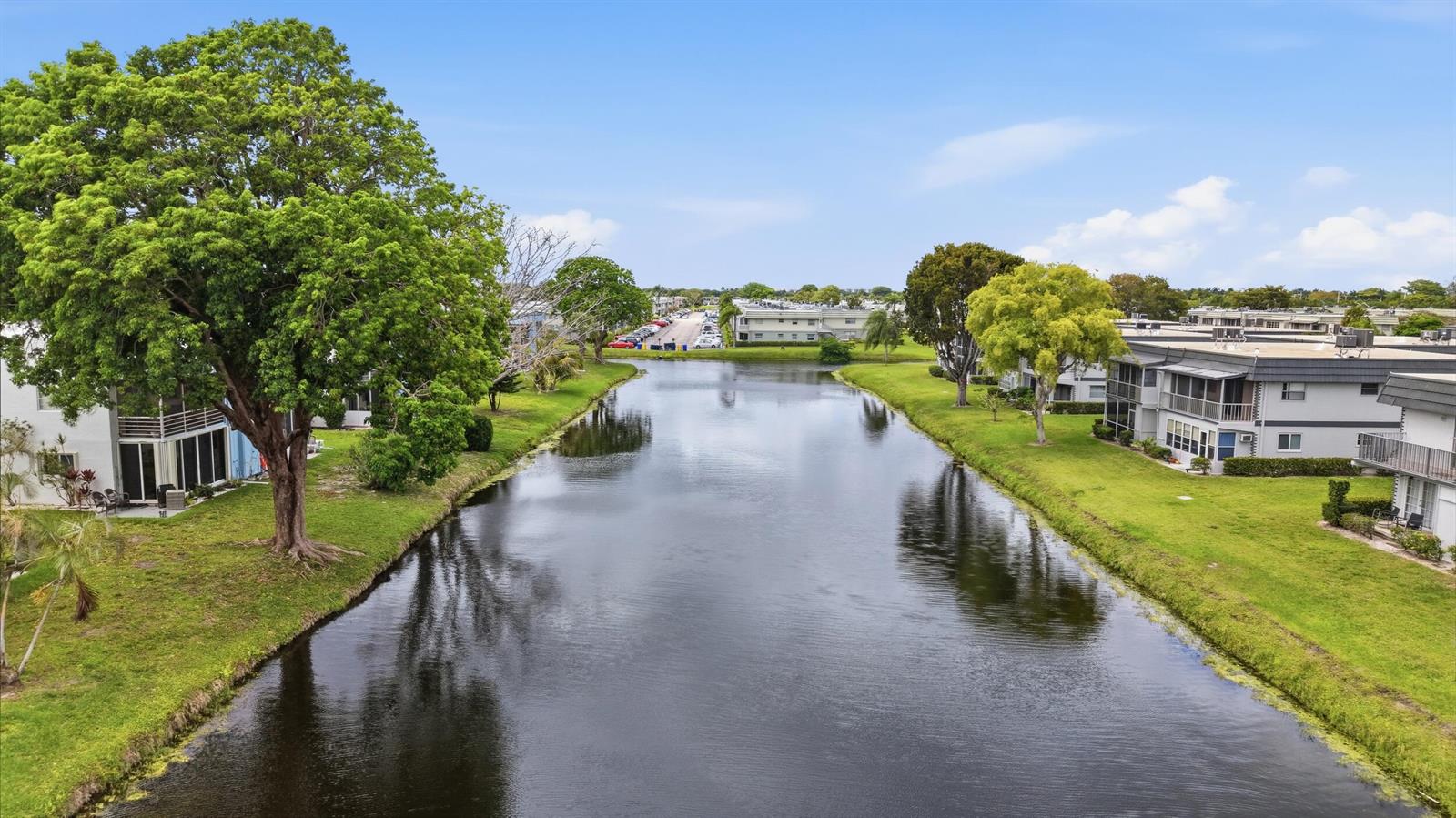 A canal flows between two rows of multi-story apartment buildings surrounded by green lawns — 376 Saxony H, Delray Beach FL 33446, DELRAY BEACH, FL